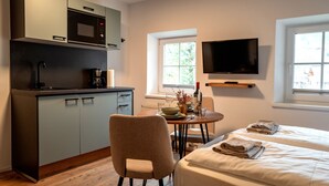 Quarto moderno com cozinha compacta, área de refeições, cama e televisão na parede.