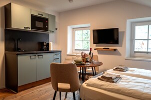 Una habitación moderna con kitchenette, comedor, cama y televisor montado en la pared.