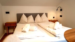 Quarto de hotel com cama de casal, duas mesas de cabeceira, cabeceira e luminária na parede.