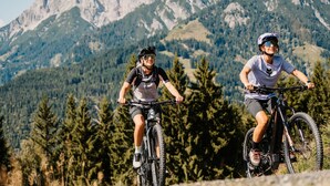 Twee mountainbikers op een pad, met een bergachtige achtergrond.