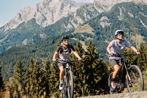 Zwei Mountainbiker auf einem Trail vor einer gebirgigen Kulisse.