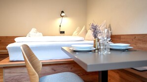 Quarto moderno com cama, mesa de cabeceira com abajur e área de refeições com mesa posta para dois.