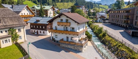 A multi-story hotel with balconies, a river running alongside, and a mountainous backdrop.