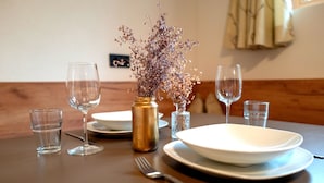 Mesa posta com pratos, copos, um vaso com flores secas e saleiro.