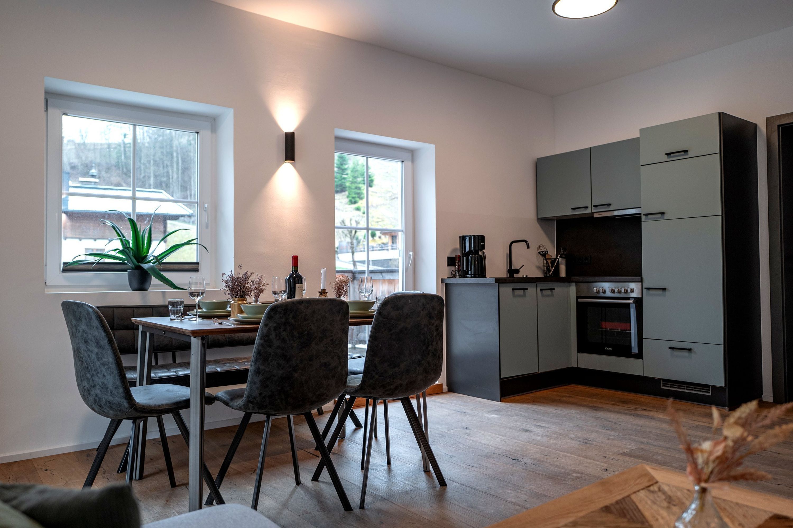 Eine moderne Küche mit grauen Schränken, einem Esstisch mit Stühlen und einem großen Fenster.