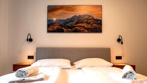 Quarto de hotel com duas camas, uma pintura com vista para as montanhas e luminárias de cabeceira.