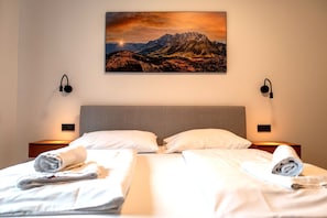 Ein Hotelzimmer mit zwei Betten, einem Gemälde mit Bergblick und Nachttischlampen.