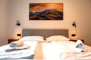 Una habitación de hotel con dos camas, un cuadro con vista a la montaña y lámparas de noche.