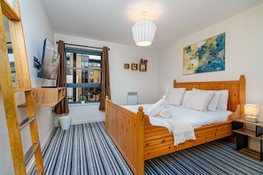 A bedroom with a wooden bed, a window with curtains, a painting on the wall, and a ladder against the wall.
