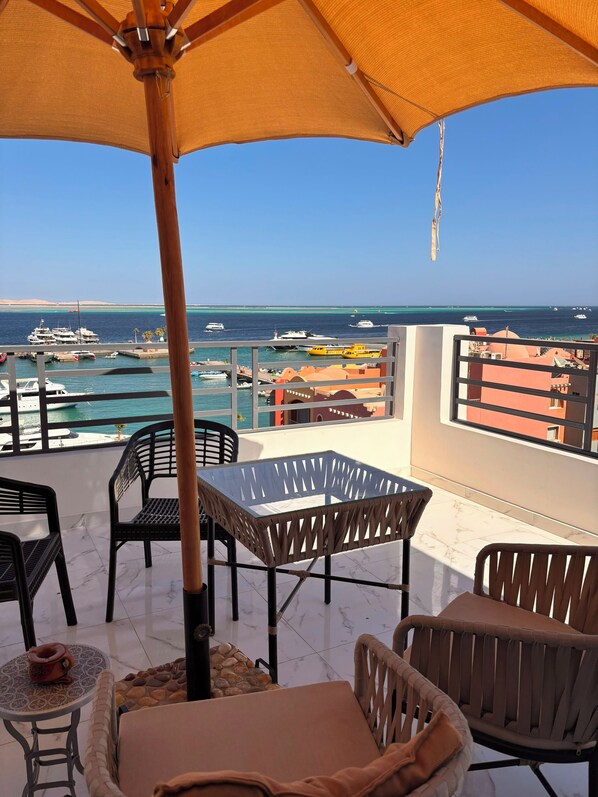 Ein Balkon mit Tisch und Stühlen, mit Blick auf einen Hafen voller Boote und einem strahlend blauen Himmel.