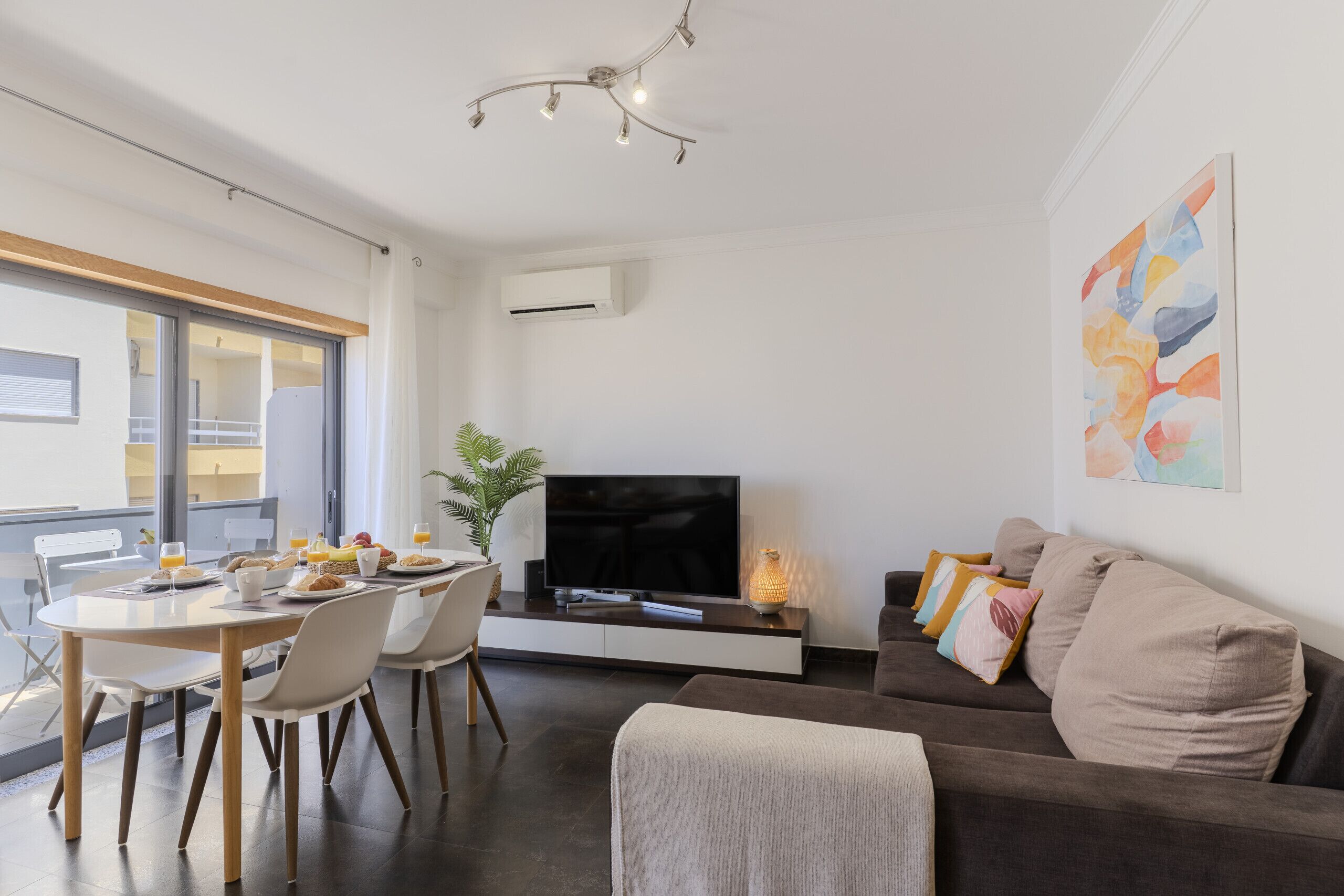 A modern living room with a dining area, a flat-screen TV, and a large window.