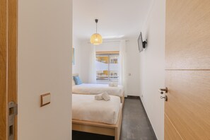 A narrow hallway leading to a room with two beds, a hanging light fixture, and a view of a building outside. - #387 Family-Friendly Apartment Near the Beach (Armação de Pêra)