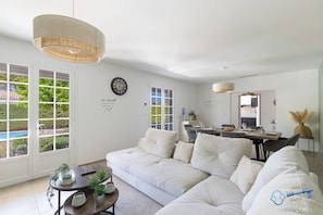 A modern living room with a sofa, dining table, and kitchen area. - L'Écrin de Provence – Villa for 8 people with a pool (Entraigues-sur-la-Sorgue)