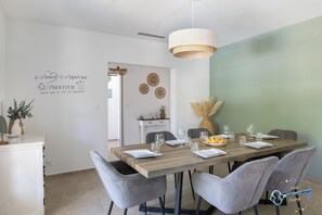 A dining area with a wooden table set for four, grey upholstered chairs, a hanging light fixture, and a decorative wall with a phrase. - L'Écrin de Provence – Villa for 8 people with a pool (Entraigues-sur-la-Sorgue)