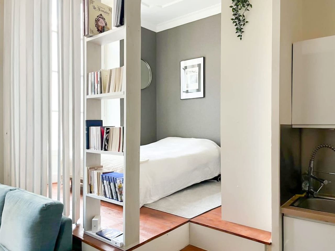 Een knus kamertje met een bed, een boekenkast en een klein keukenhoekje.