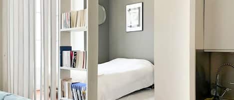 A compact room with a bed, a bookshelf, and a small kitchen area.
