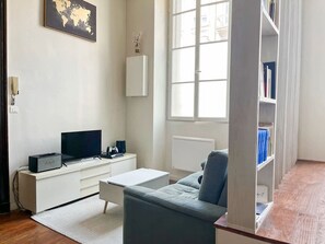A modern living room with a flat-screen TV, a white entertainment unit, a grey sofa, and a bookshelf. - Charming Studio in the Heart of Bordeaux (Bordeaux)