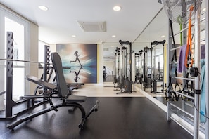 Ein Fitnessraum mit unterschiedlichen Trainingsgeräten, einem großen Spiegel und einem Wandgemälde.