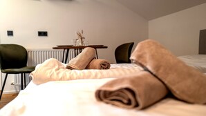 Quarto de hotel com uma cama, duas cadeiras, uma mesinha com um vaso e um radiador.