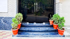 A building entrance with a black door, two potted plants on the steps, and a brick wall. - Super Collection O Hingna Road (Nagpur)