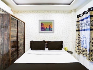A hotel room with a bed, two pillows, a framed picture on the wall, a wardrobe, and curtains.