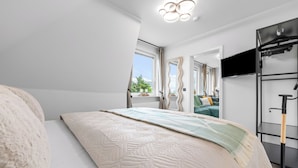 A modern bedroom with a bed, a large mirror, a TV, and a window. - Modern, newly renovated vacation rental in the heart of Hörnum on SyltModern, newly (Hörnum (Sylt))