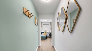 A hallway with a light green wall, wooden coat hooks, a framed picture, and a large gold-framed mirror. - Modern, newly renovated vacation rental in the heart of Hörnum on SyltModern, newly (Hörnum (Sylt))