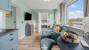 A modern living room with a sofa, a dining area, a TV, and a window with a view. - Modern, newly renovated vacation rental in the heart of Hörnum on SyltModern, newly (Hörnum (Sylt))