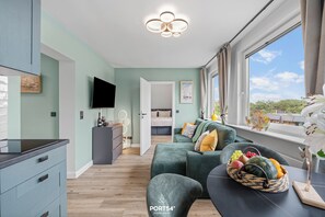 Ein modernes Wohnzimmer mit Sofa, Essbereich, Fernseher und Fenster mit Aussicht.