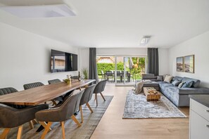 A modern living room with a dining area, a sofa, and a TV mounted on the wall. - Aquamarin Holiday Apartment: Fully Renovated, Family-Friendly and Dog-Friendly f (Westerdeichstrich)