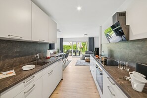 Eine moderne Küche mit einer zentralen Kochinsel, weißen Schränken und Blick auf eine Terrasse.