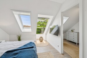 Ein Schlafzimmer mit Bett, Fernseher, Kommode und Fenster.