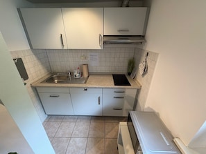 Eine kleine Küche mit weißen Schränken, einem Edelstahl-Spülbecken, einer schwarzen Arbeitsplatte und einem eingebauten Backofen.
