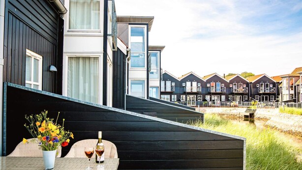 A modern outdoor seating area with a table and chairs, a potted plant, and a bottle of wine. - 5 Star Holiday Home in Juelsminde (Juelsminde)