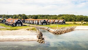 A row of black buildings with red roofs, a small bridge, and a calm body of water. - 5 Star Holiday Home in Juelsminde (Juelsminde)