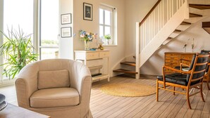 A room with a sofa, a chair, a desk, a staircase, and a view through a window. - 5 Star Holiday Home in Juelsminde (Juelsminde)