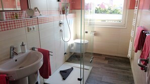 Ein Badezimmer mit Duschkabine aus Glas, einem weißen Waschbecken und einem roten Handtuch.