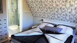Ein Schlafzimmer mit Bett, Nachttisch, Kommode und einer Duschkabine.