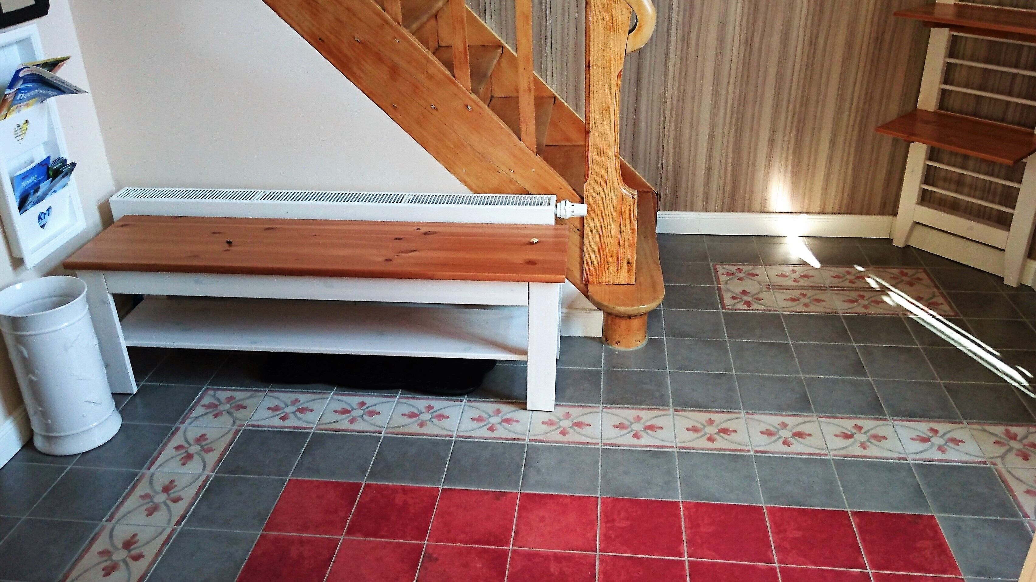 Eine Treppe mit Holzgeländer, einer weißen Bank und einem gefliesten Boden mit rotem und grauem Muster.