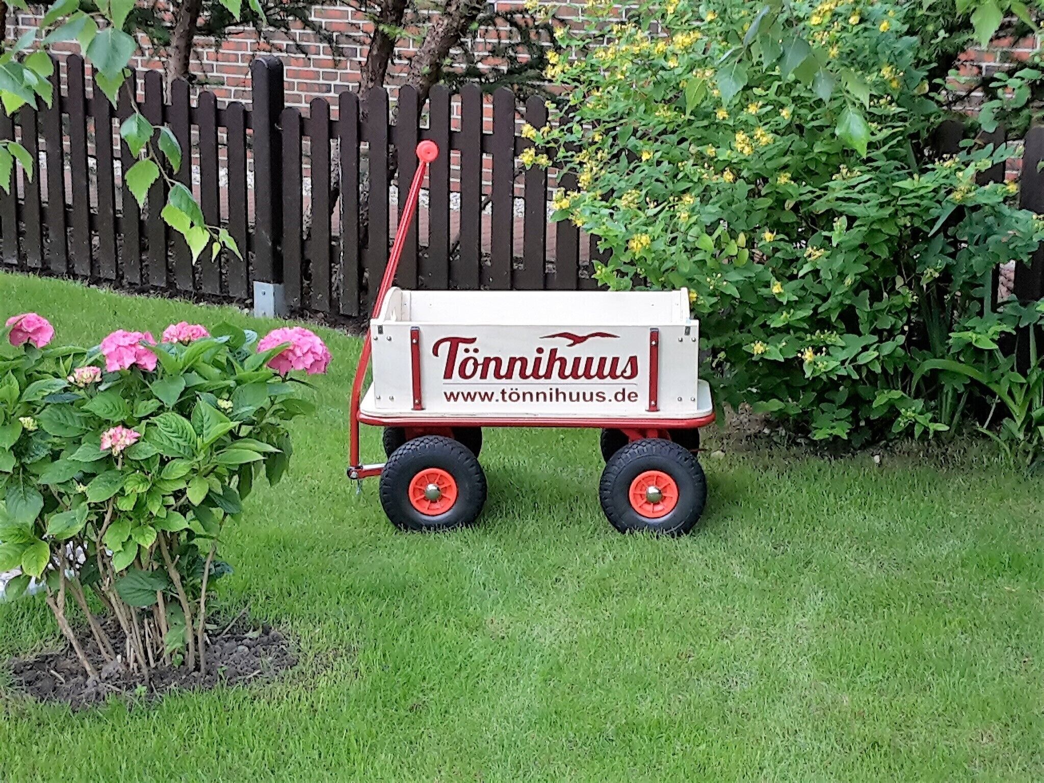 Ein Garten mit einem Schubkarren mit dem Aufdruck 'Tönnihuus' und einer Backsteinmauer im Hintergrund.
