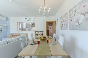 Ein Essbereich mit einem für vier Personen gedeckten Tisch, Stühlen, einer Kronleuchter und Wandbildern.
