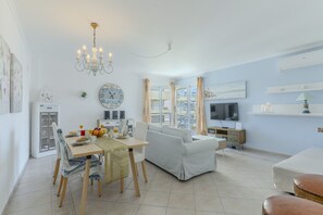 Ein modernes Wohnzimmer mit Essbereich, einer Couch, einem Fernseher und einer Chandelüster.