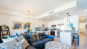 A modern living room with a blue sofa, patterned ottoman, and artwork on the wall. - Modern Bayfront Condo with Pool & Balcony View (Sarasota)