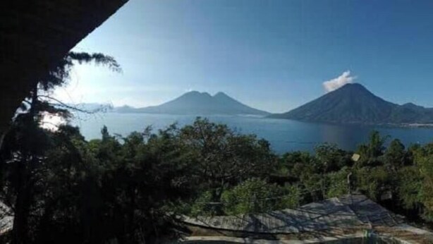 A view from a covered outdoor area with a mountain and a body of water in the background. - Eco Domo. (San Marcos La Laguna)
