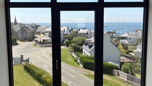 A large arched window with a view of a coastal town, a road, and a church. - Avel Vor - Family home, renovated, sea view (Porspoder)