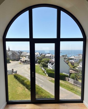 Ein großes Bogenfenster mit Blick auf eine Küstenstadt, eine Straße und eine Kirche.