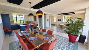A modern dining area with a long table, red chairs, and black pendant lighting. - Avel Vor - Family home, renovated, sea view (Porspoder)