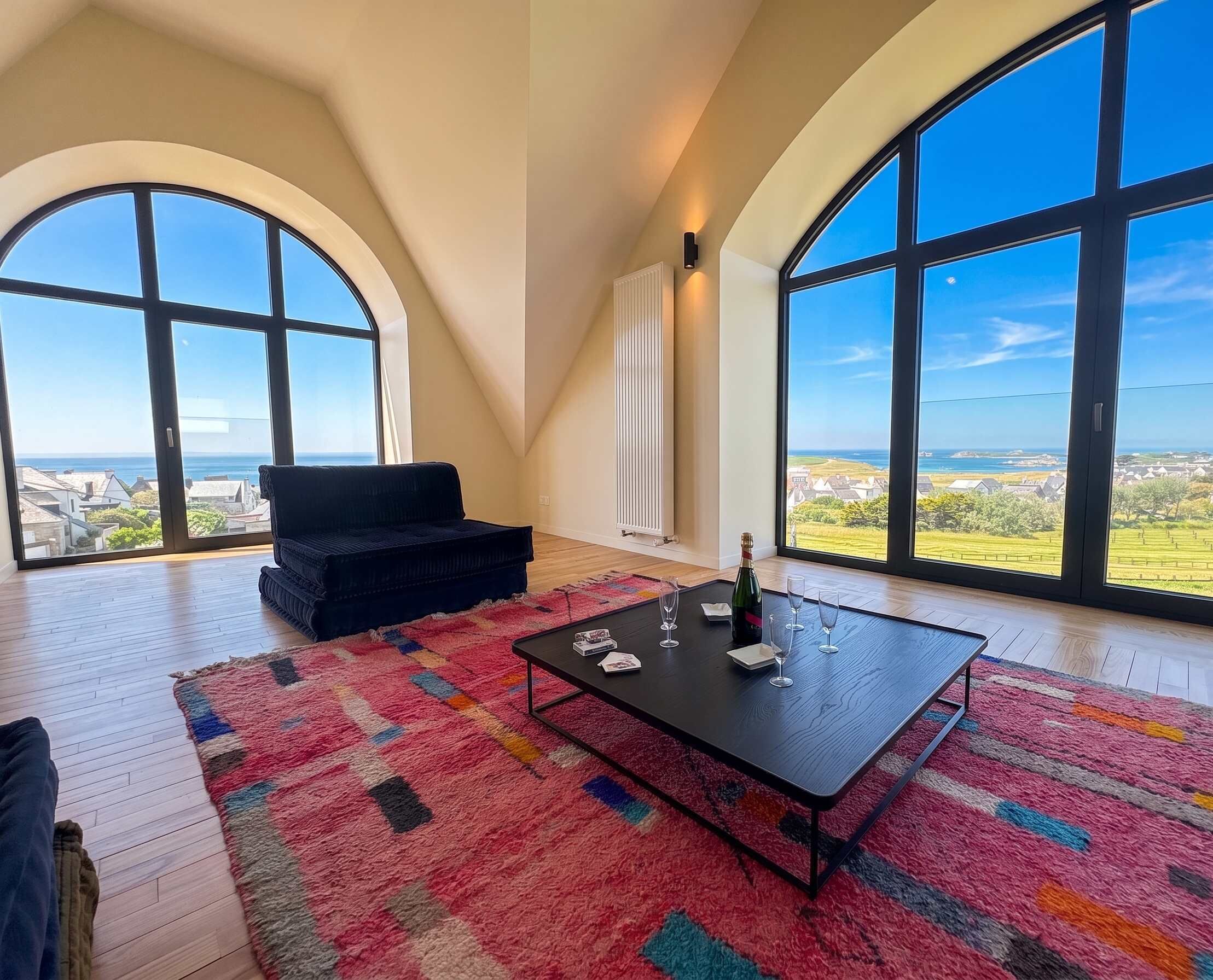 A spacious room with large arched windows, a black sofa, a coffee table, and a colorful rug.