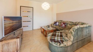 A living room with a flat-screen TV, a sofa with a blanket, a coffee table, and a hanging light fixture. - Family-friendly vacation rental with a terrace and Wi-Fi—close to the beach in a quiet location (Koserow)