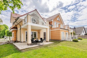 Ein zweistöckiges Haus mit Balkon, einer Terrasse mit Gartenmöbeln und einem gepflegten Rasen.